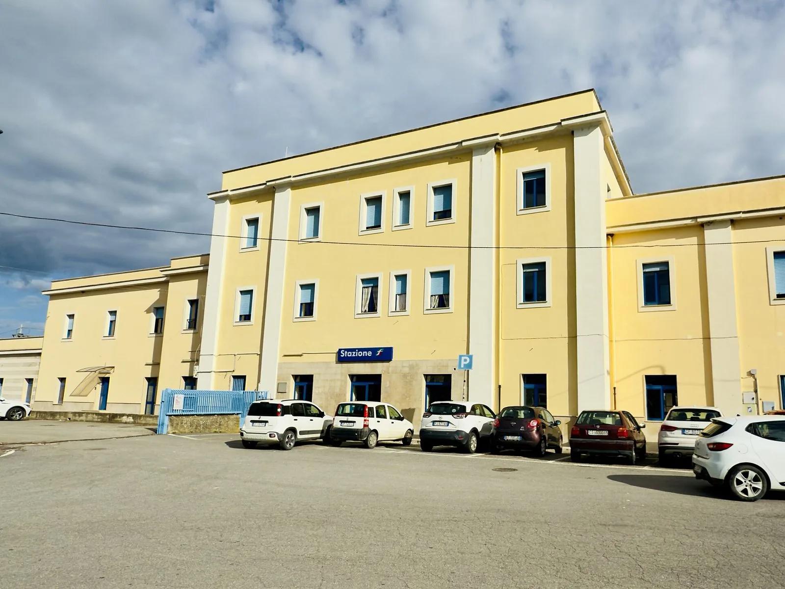 Il fabbricato viaggiatori color giallo chiaro della stazione ferroviaria di Sibari, con l'insegna Stazione e auto parcheggiate sul piazzale