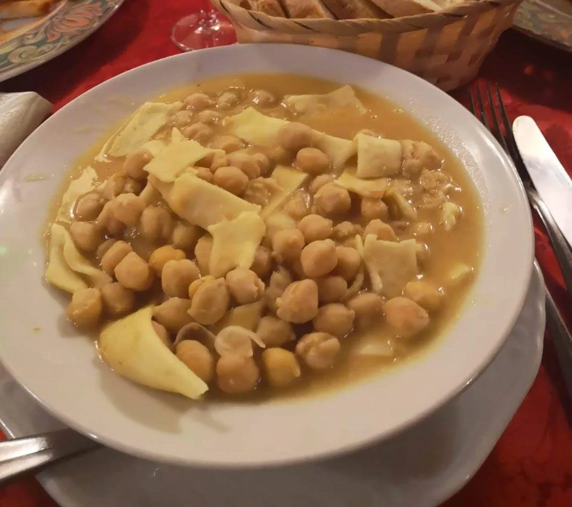 Un piatto fondo di lagane e ceci alla cosentina: pasta larga fatta in casa con ceci nel loro brodo, su una tovaglia rossa