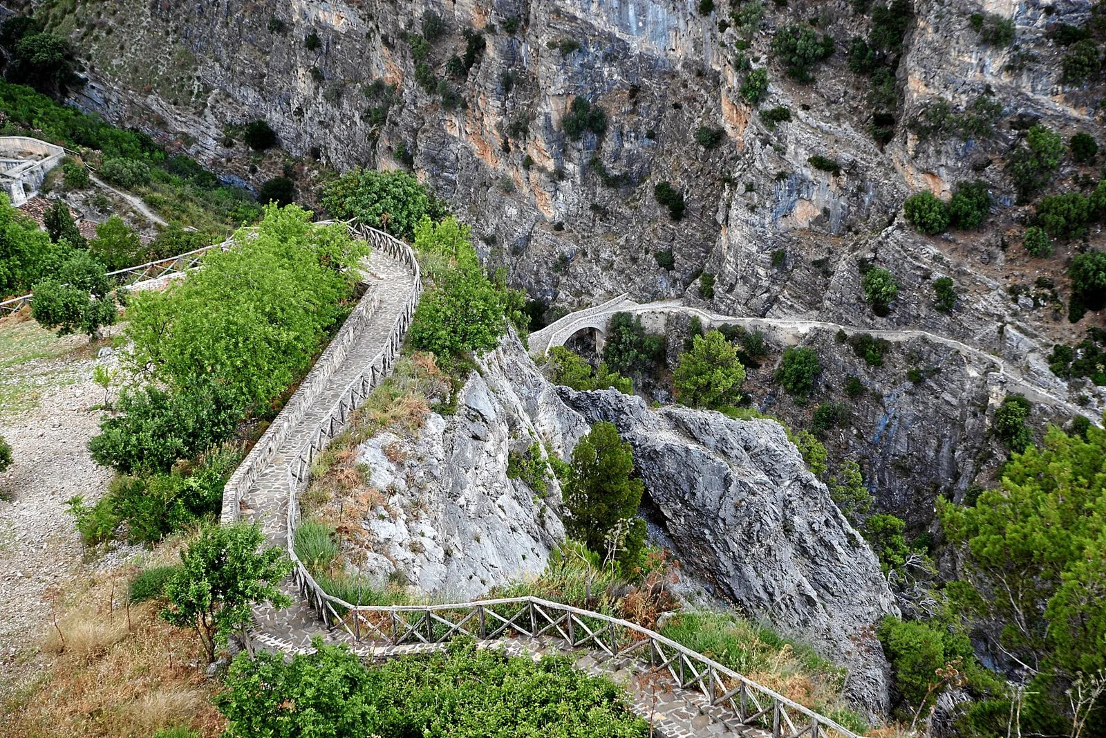 Il Ponte del Diavolo a una sola arcata sul fondo delle Gole del Raganello, visto dal belvedere di Civita con il sentiero lastricato che scende tra le rocce